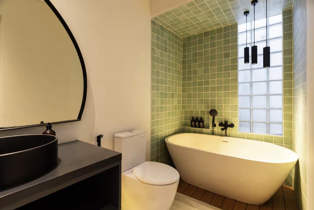 Bathroom with green tiled wall, freestanding tub and round mirror