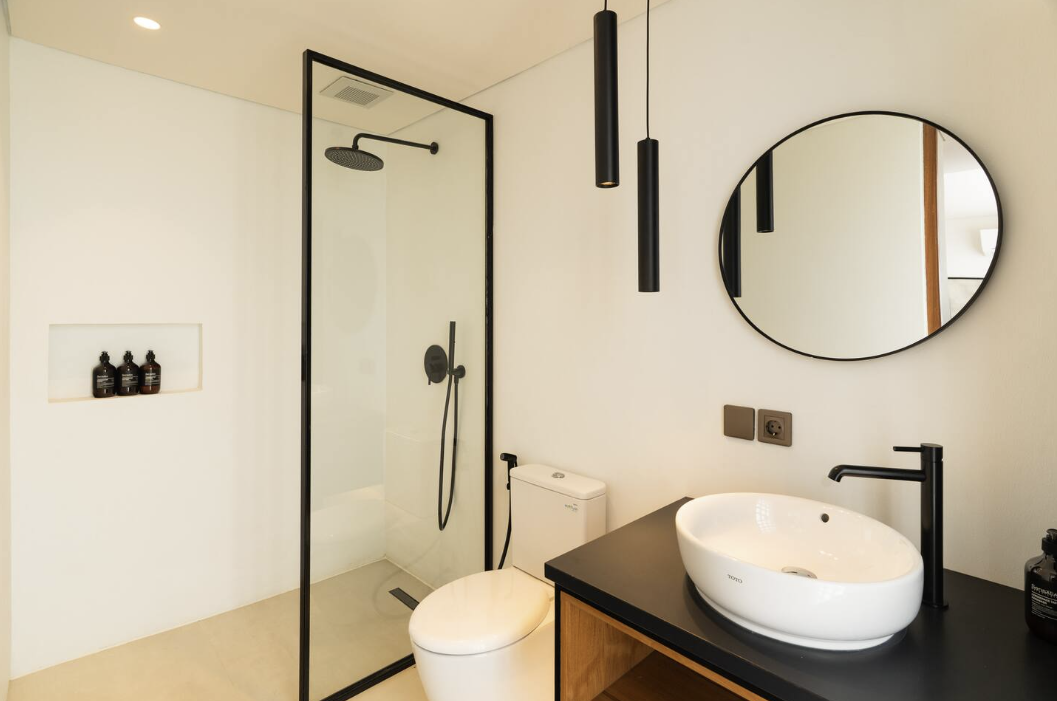 Bathroom with glass-enclosed shower, round mirror and black vanity